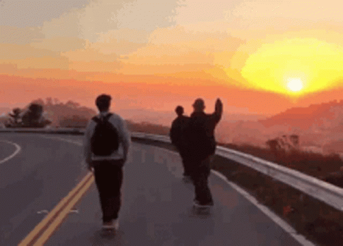 Three People Are Walking Down A Road At Sunset GIF