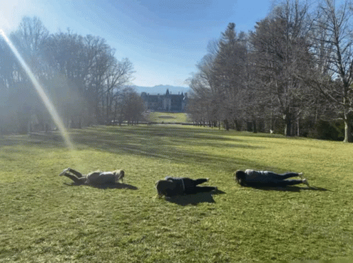 Three People Laying In Grassy Field With Large House GIF