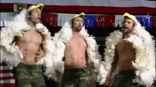 Three Shirtless Men Are Standing Next To Each Other Wearing Feather Boa Jackets . GIF