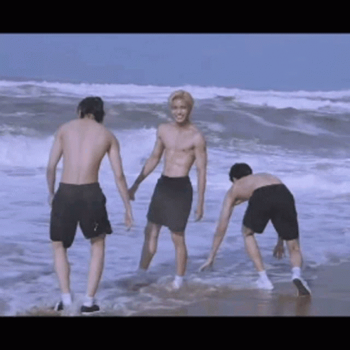 Three Shirtless Men Are Standing On The Beach Holding Hands GIF