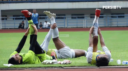 Three Soccer Players Stretch Their Legs On A Field With Persibtv Written In The Corner GIF