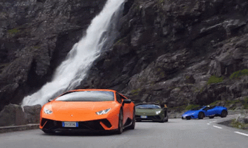 Three Sports Cars Are Driving Down A Road Near A Waterfall GIF