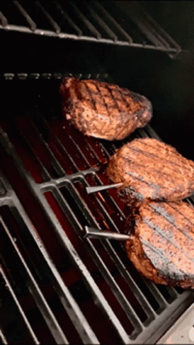 three steaks are cooking on a grill with a red sauce