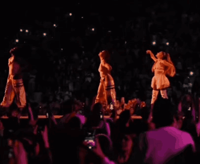 Three Women Are Dancing On A Stage In Front Of A Crowd In A Dark Room . GIF