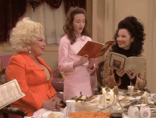 Three Women Are Sitting At A Table Looking At A Menu GIF
