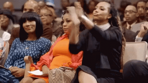 Three Women Are Sitting In A Crowd Of People And One Of Them Is Taking A Picture Of Herself With Her Phone . GIF