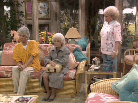 Three Women Are Sitting In A Living Room With Wicker Furniture GIF