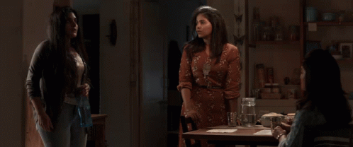 Three Women Are Standing Around A Table With A Pitcher Of Water On It GIF