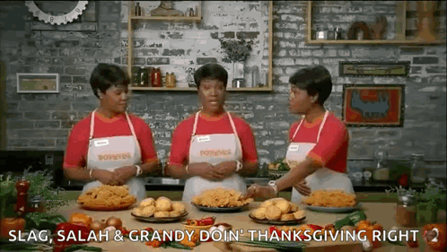 Three Women Are Standing In A Kitchen With Plates Of Food On The Table . GIF