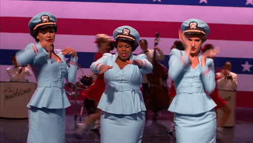 Three Women in Blue Uniforms Dancing in Front of Band
