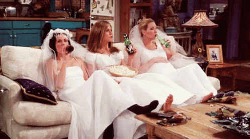 Three Women In Wedding Dresses Sit On A Couch Drinking Beer GIF