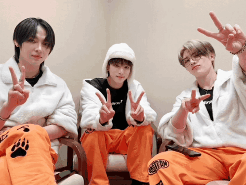 Three Young Men Are Sitting In Chairs Giving The Peace Sign And One Of Their Pants Says One Team GIF