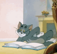 Tom From Tom And Jerry Is Laying On The Floor Reading A Book GIF