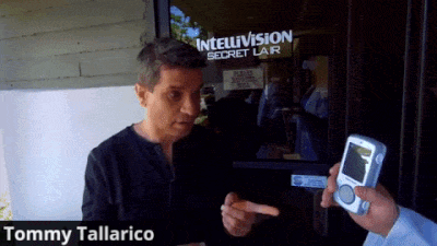 Tommy Tallarico Is Holding A Cell Phone In Front Of An Intelvision Secret Lair GIF