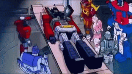 Transformers Standing Around Robot Laying on Bed