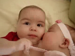 Two Babies Are Kissing Each Other On The Cheeks . GIF