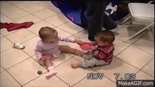 Two Babies Are Sitting On A Tiled Floor Playing With Toys . GIF