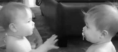 Two Babies Are Standing Next To Each Other And Looking At Each Other In A Black And White Photo . GIF