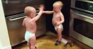 Two Babies In Diapers Are Standing Next To Each Other In A Kitchen And Giving Each Other A High Five . GIF
