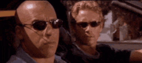 Two Bald Men Wearing Sunglasses Are Looking At Something GIF