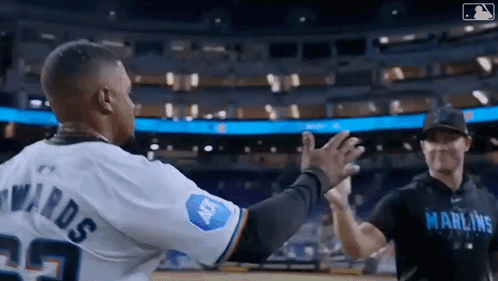 Two Baseball Players Are Giving Each Other A High Five On A Field . GIF