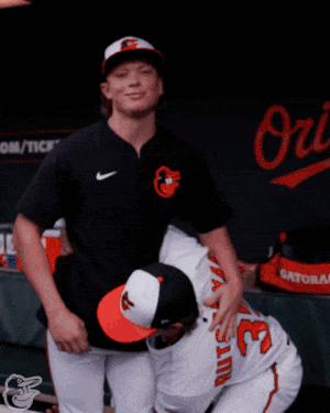 Two Baseball Players Are Hugging Each Other In Front Of A Sign That Says Orioles GIF