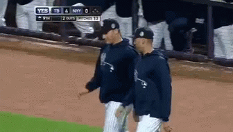 Two Baseball Players Are Walking On A Field With A Scoreboard Behind Them That Says Yes GIF
