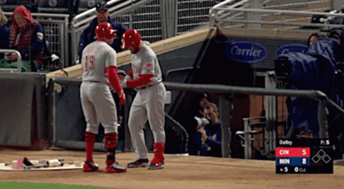 Two Baseball Players Standing On A Field With A Carrier Sign Behind Them GIF