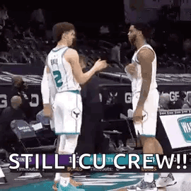 two basketball players are standing next to each other on the court talking to each other .