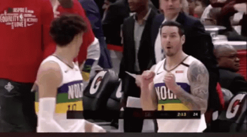 Two Basketball Players Are Talking To Each Other On The Court While A Man In A Suit Stands Behind Them . GIF