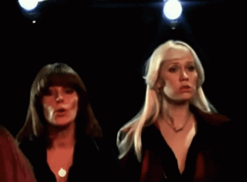 Two Blonde Women Are Standing In A Dark Room GIF