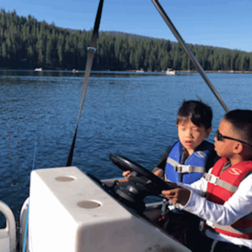 Two Boys Wearing Life Jackets Are Sitting On A Boat GIF