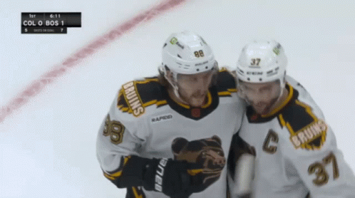 Two Bruins Hockey Players On The Ice With A Scoreboard In The Background GIF