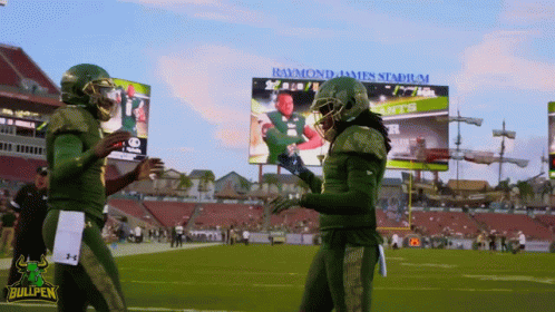 Two Bullpen Football Players Shake Hands in Front of Raymond James Stadium Billboard