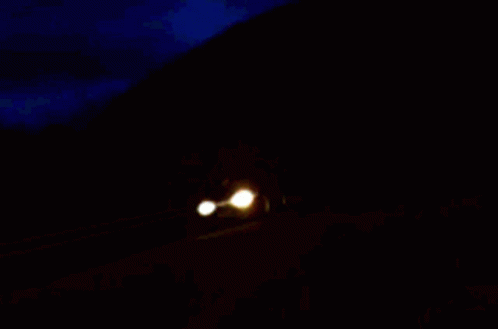 Two Cars Are Driving Down A Road At Night GIF