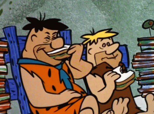 Two Cartoon Characters Eating Sandwiches Next To A Pile Of Books GIF