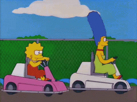 Two Cartoon Characters , Lisa Simpson And Marge Simpson , Are Driving Go Karts On A Track . GIF