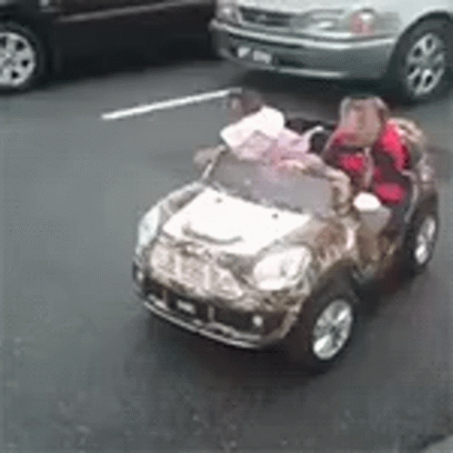 Two Children Are Riding In A Toy Car On The Street GIF