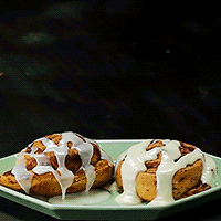 Two Cinnamon Rolls With White Frosting On A Plate GIF