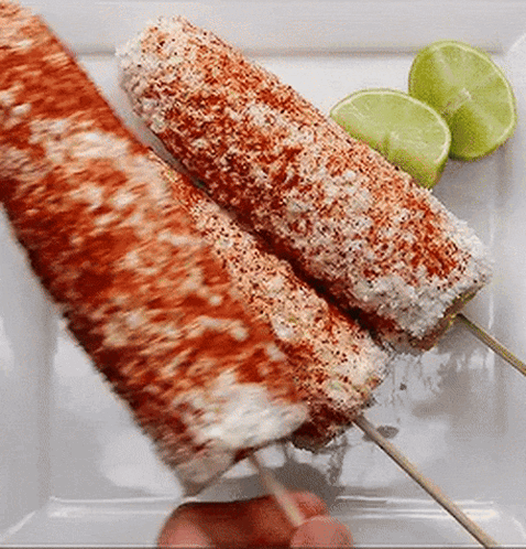 Two Corn On The Cob On Skewers On A White Plate With Limes . GIF