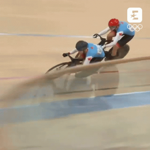 Two Cyclists Are Racing On A Track With The Olympics Logo GIF