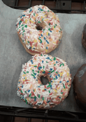 Two Donuts With Sprinkles On Them Are On A Table GIF