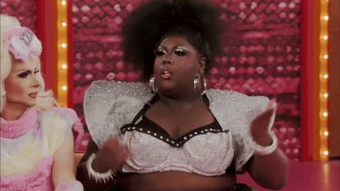Two Drag Queens Are Sitting Next To Each Other And One Of Them Is Wearing A Bra With Pearls On It GIF