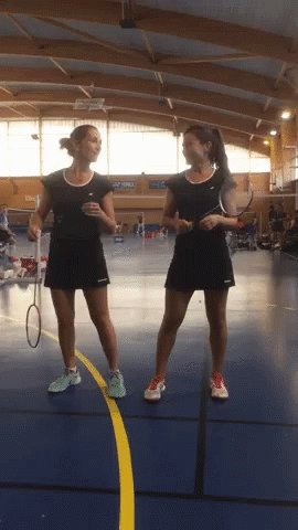 Two Female Badminton Players Standing Next To Each Other On A Blue Court GIF