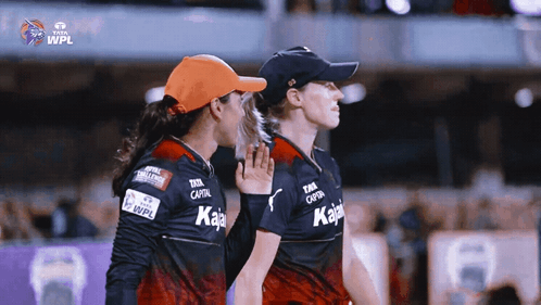 Two Female Cricket Players Standing Next To Each Other With The Wpl Logo On The Bottom GIF