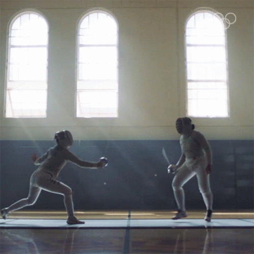 Two Female Fencers Are Fighting In A Gym With The Olympics Logo In The Background GIF