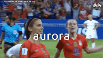 Two Female Soccer Players Are Standing On A Field And The Word Aurora Is On The Screen . GIF