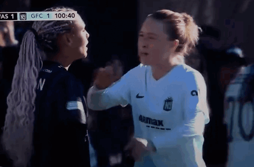 Two Female Soccer Players Hugging in Front of Scoreboard Saying GFC 1