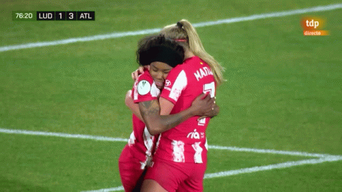 Two Female Soccer Players Hugging on Field with TDP Ad