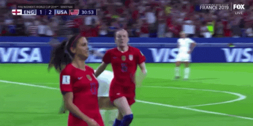 Two Female Soccer Players On A Field With Visa Advertisements Behind Them GIF